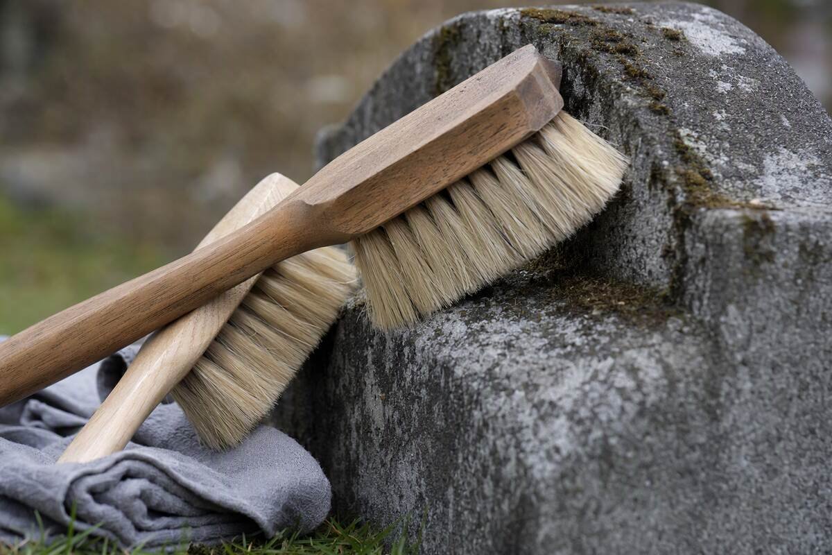Soft brushes carefully removing moss from the edge of a granite memorial